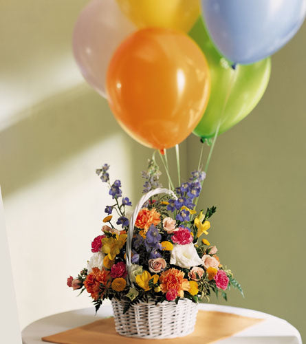 Colours Abound Arrangement - colourful floral design in a white basket with colourful balloons.