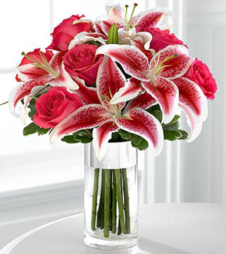 Bouquet of pink roses and stargazer lilies in a clear vase.