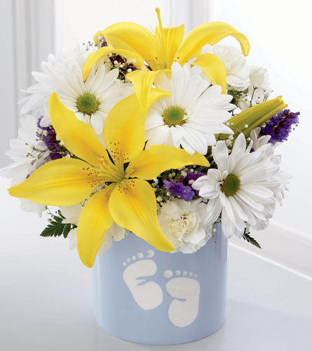 Bouquet with yellow lilies, white daisies featuring purple highlights in a blue container with baby footprints.