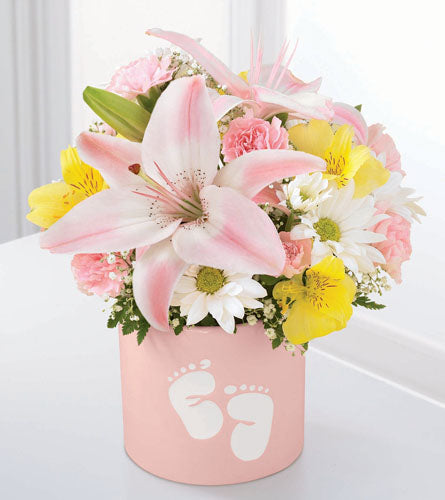Bouquet of lilies, mini carnations and daisies in a pink container with baby feet printed on it.