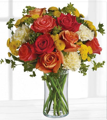 Citrus Kissed - bouquet of red, orange, and yellow flowers in a clear vase.