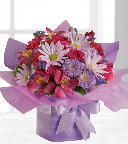 Teleflora's Lovely Lavender Present - arrangement of colourful flowers wrapped in purple paper with a white ribbon.