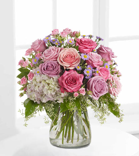 Your Light Shines - bouquet of pink. purple and white flowers with greenery in a clear glass vase.