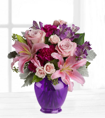 Elegant Beauty - Bouquet of pink roses and lilies with a mix of purple flowers in a purple glass vase.