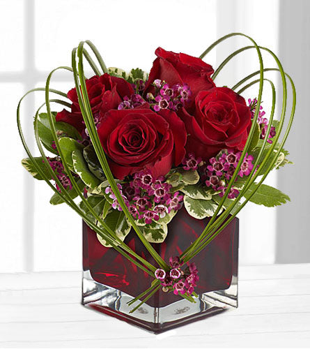 Sweet Thoughts - Heart-shaped flower arrangement with red roses, purple waxflower and greenery in a red glass cube.