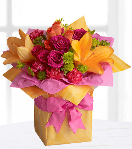 Tres Chic Present - colourful mixed flowers in a glass cube vase wrapped in yellow paper with a pink bow.