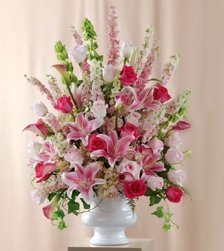 Funeral floral arrangement with pink and white flowers in a white vase.