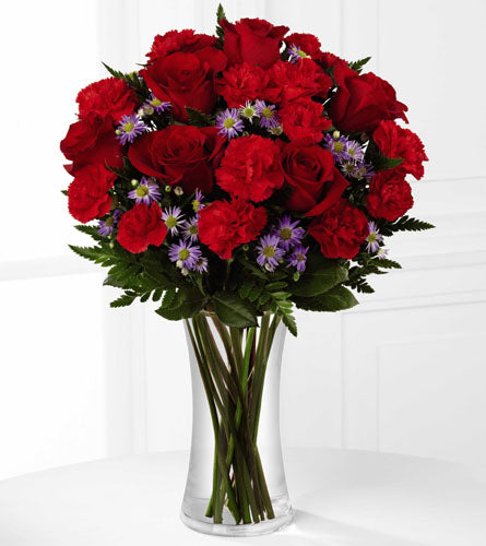 Love Is Here To Stay - Bouquet of red roses and carnations with purple flowers in a clear glass vase.