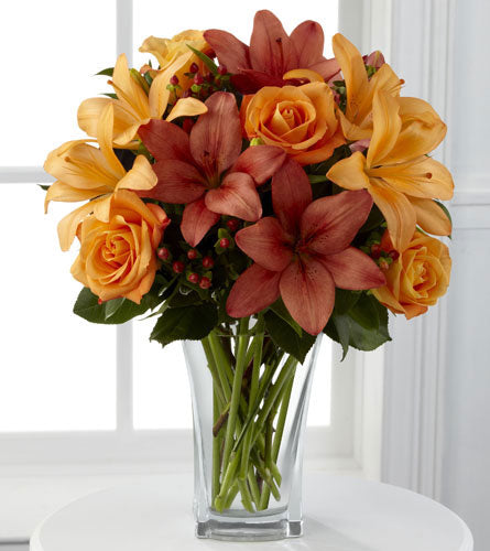 Arrangement of orange and peach flowers in a clear glass vase.