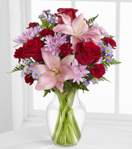 Irresistible Love Bouquet - colourful mix of red, purple and pink flowers in a clear glass vase.