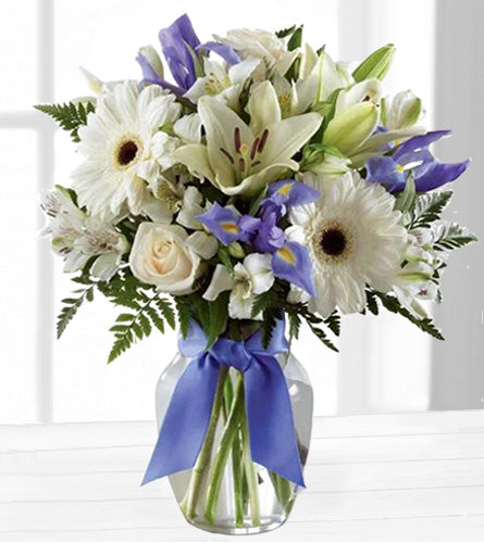 Miracle's Light - Bouquet of white and purple flowers in a clear vase with a blue ribbon.