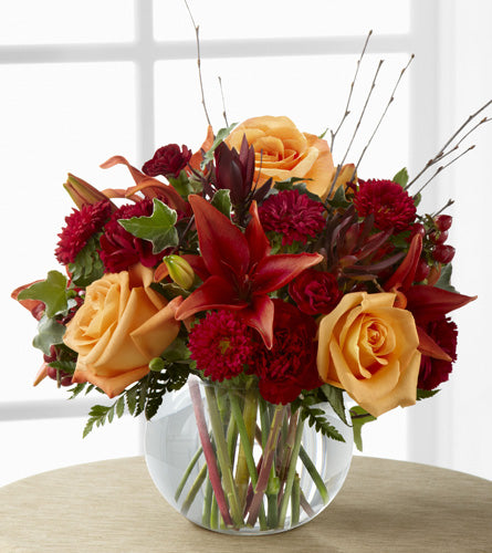 Bouquet of orange roses with a mix of colourful flowers  in a clear bubble bowl vase 