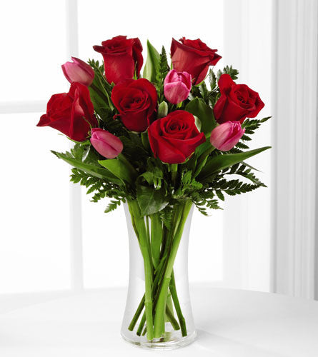 The Love Wonder Bouquet - red roses and pink tulips with a mix of greens in a clear vase.