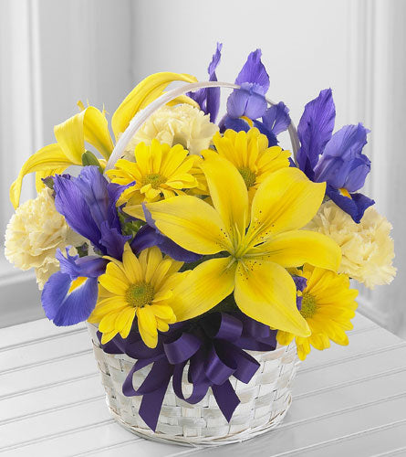 Spirit of Spring Basket - arrangement of yellow and purple flowers in a white basket with a purple bow.