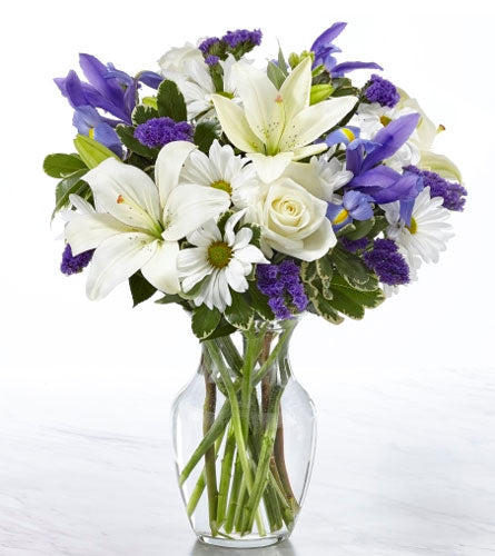 Sincerest Blessings Bouquet - arrangement of white lilies, purple iris, daisies and greenery in a clear vase.