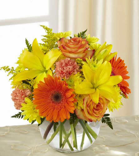 Vibrant Views Bouquet - arrangement of orange roses and gerbera daisies arranged with yellow lilies and other mixed flowers in a clear, bowl shaped vase.