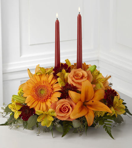 FTD's Bright Autumn Centrepiece - floral arrangement with orange and yellow flowers and two red candles.