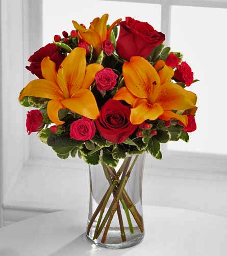 Happy Thoughts Bouquet - floral arrangement  of red roses, pink spray roses and orange lilies in a clear vase.