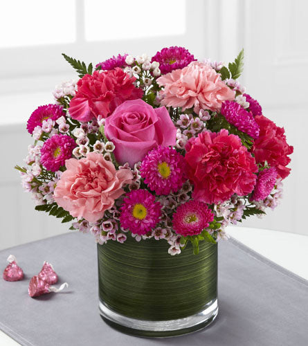 Pink Pursuits Bouquet - arrangement of pink roses, carnations and asters in a glass, leaf wrapped cylinder vase.