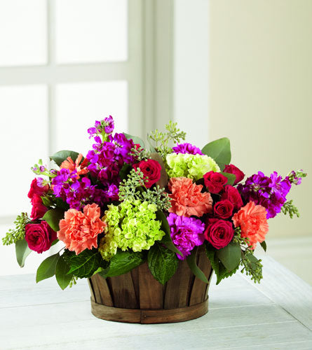 New Surprise - colourful flower arrangement in a brown wooden basket.