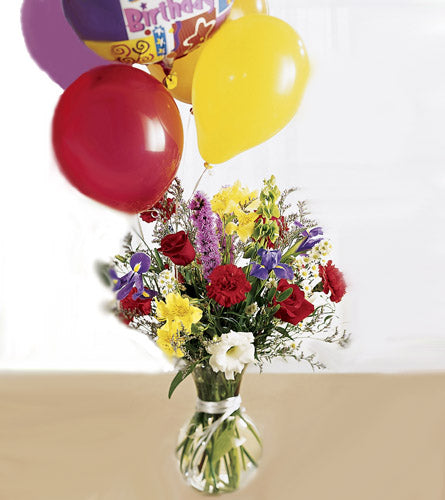 Arrangement of colourful mixed flowers in a clear vase with balloons.