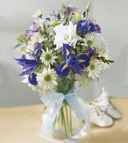Bouquet of flowers with blue and white flowers in a clear glass vase.