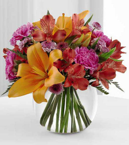 FTD's Light of My Life Bouquet - mix of orange, red and pink  flowers displayed in a clear glass bowl.