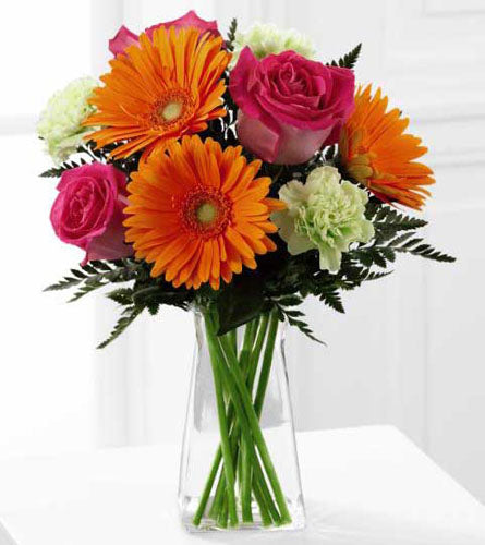 Pure Bliss - Floral arrangement of pink roses, orange gerbera daisies and pistachio carnations placed in a clear glass vase.