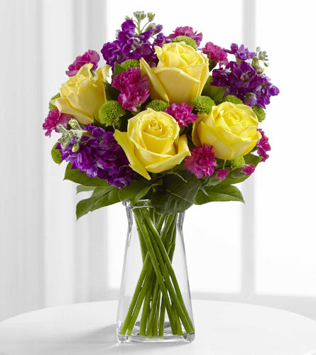 FTD's Happy Times Arrangement - yellow roses as well as purple and pink flowers placed in a clear glass vase.
