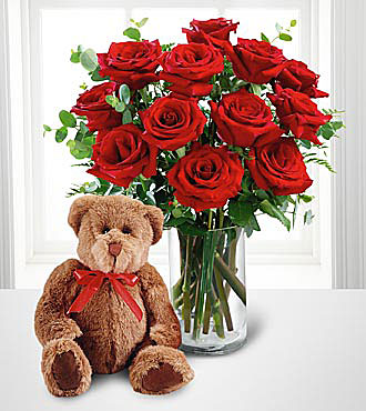 FTD's Red Roses and Hugs Bouquet - twelve red roses arranged in a clear glass vase with a brown bear wearing a red bow.