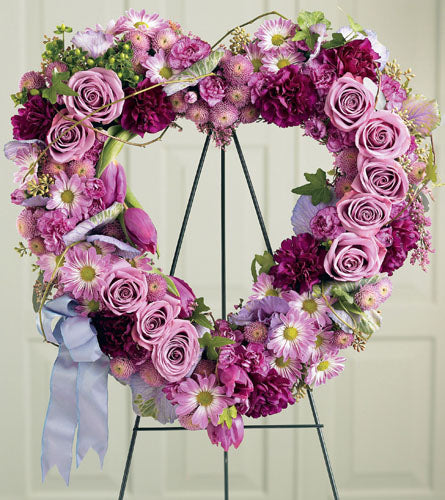 Heartfelt Sympathies Wreath - floral heart shaped wreath with pink roses and purple carnations flowers on a stand.