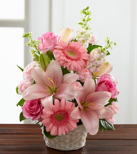 Whispering Love Arrangement - mixed pink flowers displayed in a white woven basket.