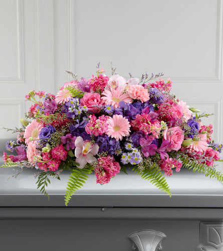 FTD's Glorious Garden Casket Spray - an arrangement of mixed pink, purple flowers displayed on top of a casket.