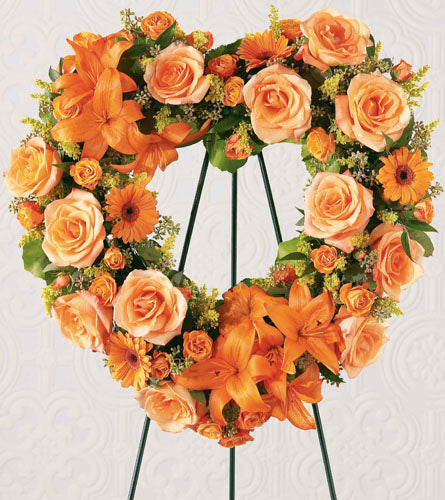 Heart's Eternal Wreath - floral heart shaped wreath with orange and peach flowers on a stand.