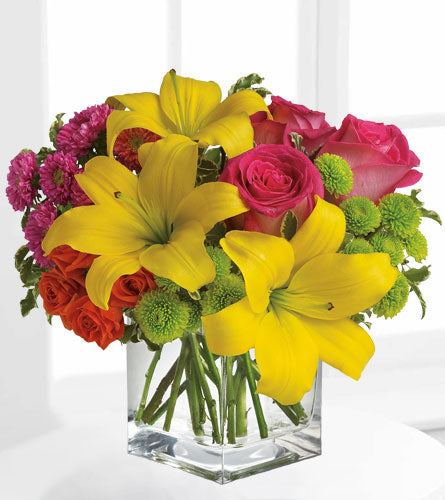 Teleflora's Sunsplash - bouquet of yellow, pink, and red flowers arranged  in a clear glass cube.