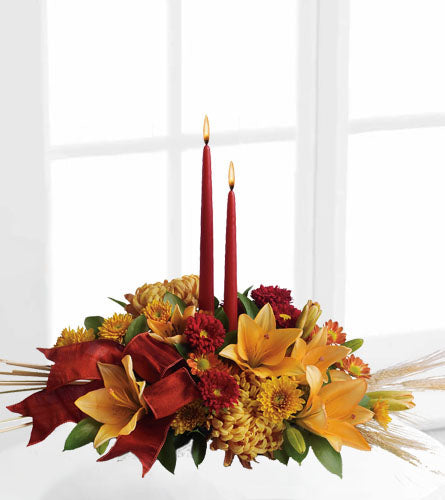 Graceful Glow Centrepiece - Decorative floral arrangement with red and yellow flowers and two red candles.