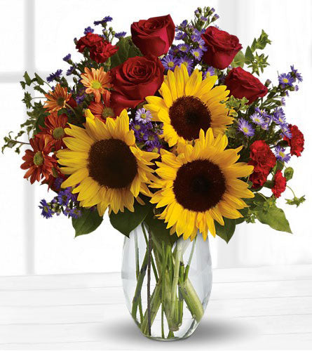 Pure Happiness - bouquet of sunflowers, red roses and colourful mixed flowers in a clear vase.