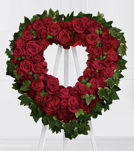 Blessed Heart - Heart-shaped wreath made of red roses and green leaves on a white stand.