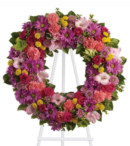Ringed by Love - colourful floral wreath on a white stand.