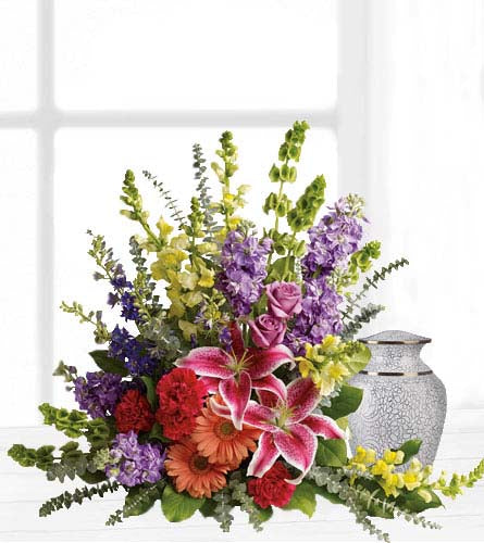 Shades of Faith - funeral arrangement of mixed colourful flowers beside a white urn.