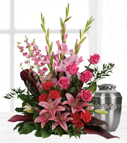 Adoring Heart - funeral arrangement of pink roses, lilies and gladioli displayed beside a silver urn.