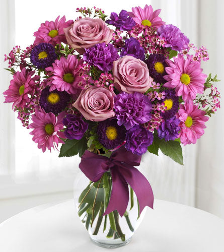 Love and Laughter in a Clear Vase - Bouquet of pink and purple flowers in a clear vase with a purple ribbon.