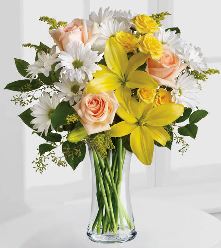 Teleflora's Daisies & Sunbeams - Bouquet of yellow lilies, white daisies, and pink roses in a clear vase.