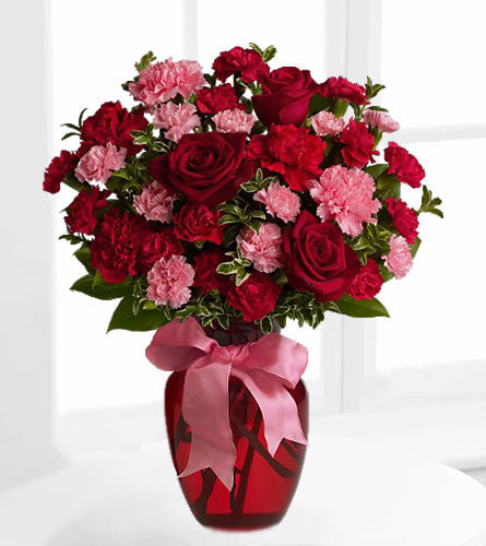 Dance With Me - Bouquet of red roses and pink carnations in a decorative. red glass vase with a pink bow.