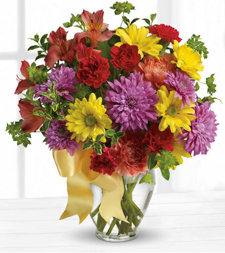 Colour Me Yours Bouquet - mixed colourful flowers in a clear glass vase with a gold ribbon.