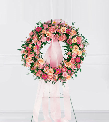 Respectful Pink Wreath - floral wreath with pink and orange flowers and a pink ribbon on a stand.