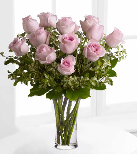 A Dozen Pale Pink Roses - bouquet of twelve pink roses with greenery in a clear vase.