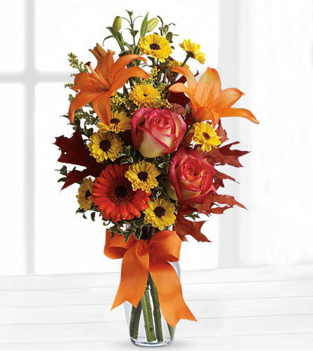 Burst of Autumn - Bouquet of autumn flowers with orange, pink and yellow in a clear vase with an orange bow.
