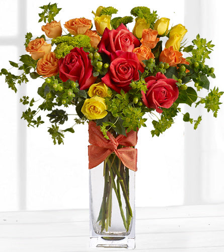 Rambling Rose - Bouquet of red, yellow, and orange roses with greenery in a clear glass vase.