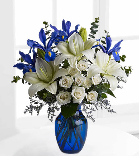 Blue Horizons Bouquet -  white lilies, roses and blue irises in a blue glass vase.